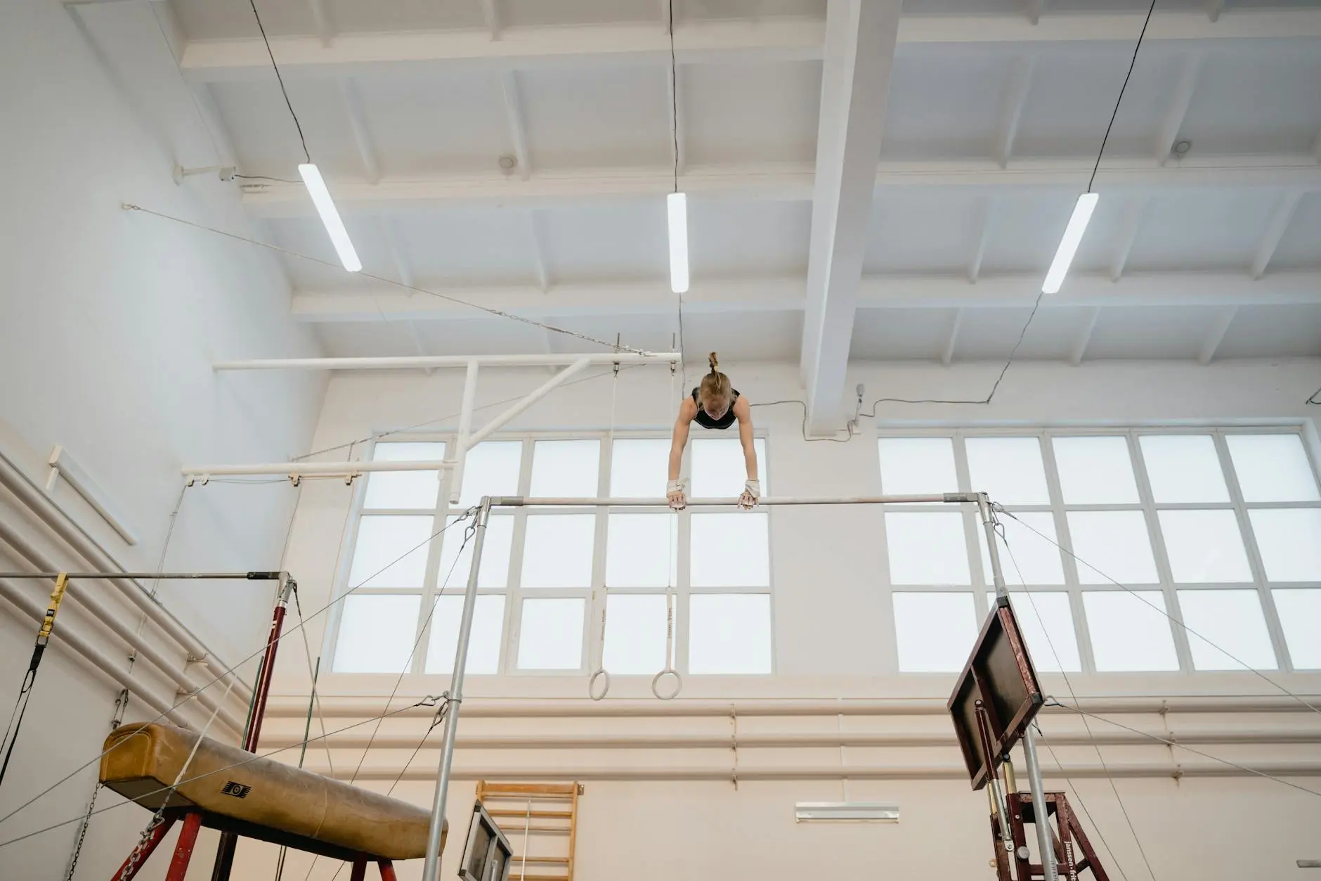 A female gymnast training on the uneven bars in a bright gym facility.