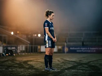 Female footballer in contemplative pose under dramatic lighting, representing pressure and scrutiny of fame