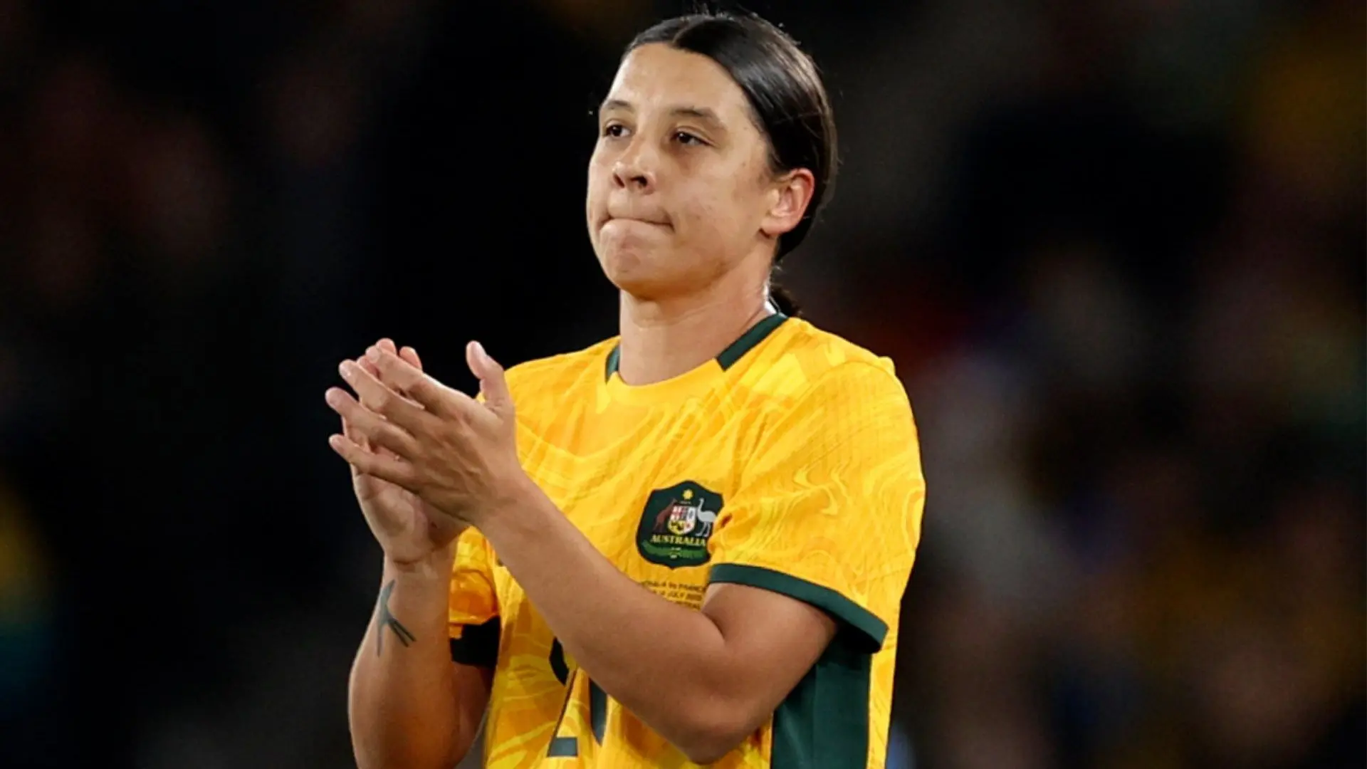Sam Kerr wearing an Australian national team jersey, clapping with a serious expression.