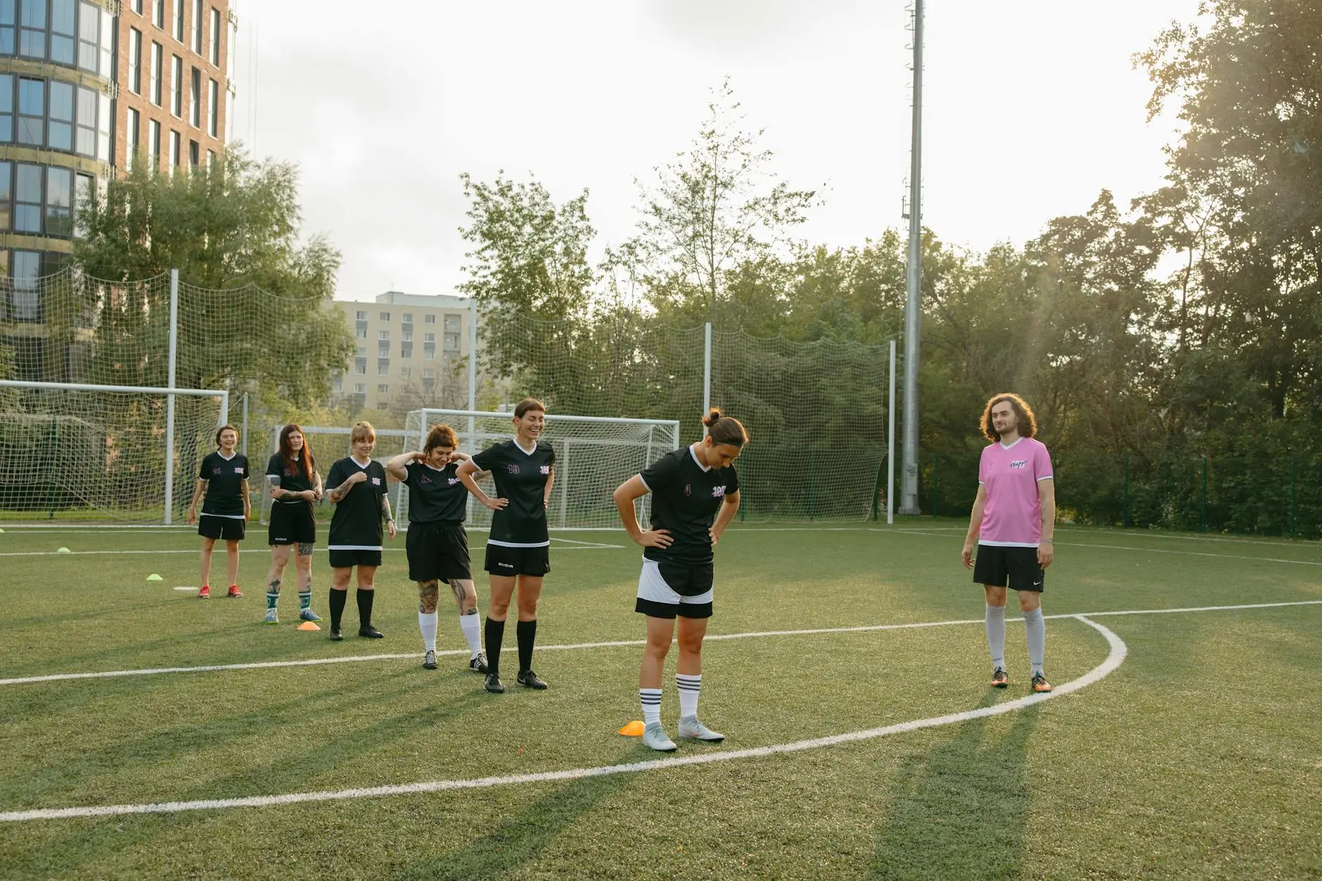Female football players in black kits practice on a training field with cones.