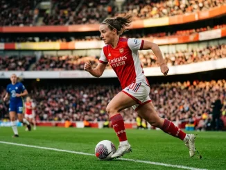 Female footballer in Arsenal red and white kit driving forward with ball on pitch in dynamic action shot