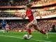 Female footballer in Arsenal red and white kit driving forward with ball on pitch in dynamic action shot