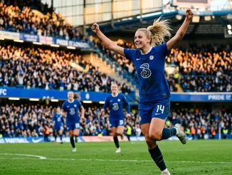 Female footballer in Chelsea kit celebrating goal in stadium with dramatic lighting