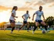 England women's footballers training intensely on pitch in white kits at golden hour