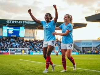 Two Manchester City women footballers celebrating on pitch in sky blue jerseys during golden hour