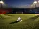 Empty floodlit stadium pitch at dusk with match ball on penalty spot, red and blue banners, dramatic shadows.