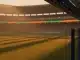 Empty floodlit stadium pitch at golden hour with packed stands, orange and blue accent lighting reflecting national colours.