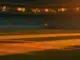 Floodlit stadium pitch at golden hour with turquoise and orange colours, dramatic shadows, packed stands blurred behind.