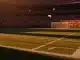 Floodlit stadium at dusk with packed stands, pristine pitch, dramatic shadows, Czech red-white and South African green-gold crowd colours.