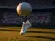 Floodlit stadium corner view with football boot and ball in motion, crowd in white and red sections, evening golden light.