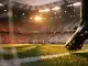 Floodlit stadium with crimson-lit stands and anonymous player boot on pitch during evening match.