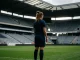 Female footballer standing alone in empty stadium, contemplative pose emphasizing isolation and emotional weight