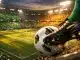 Close-up of a football boot striking a ball on a floodlit pitch, with emerald and gold-lit stadium stands blurred in background.