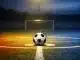 Floodlit football pitch at dusk with match ball on centre spot, dramatic lighting and split colour palette.