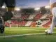 Floodlit stadium with crimson and white stands; motion-blurred footballer's boot and ball on illuminated pitch.