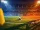 Empty floodlit stadium pitch at dusk with match ball on centre spot, blue-yellow and red-ochre lighting, dramatic shadows.