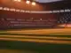 Floodlit stadium pitch at golden hour with national colour palette, dramatic shadows, packed stands in background