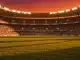 Floodlit stadium at dusk with packed stands and dramatic golden-hour lighting, no players visible.