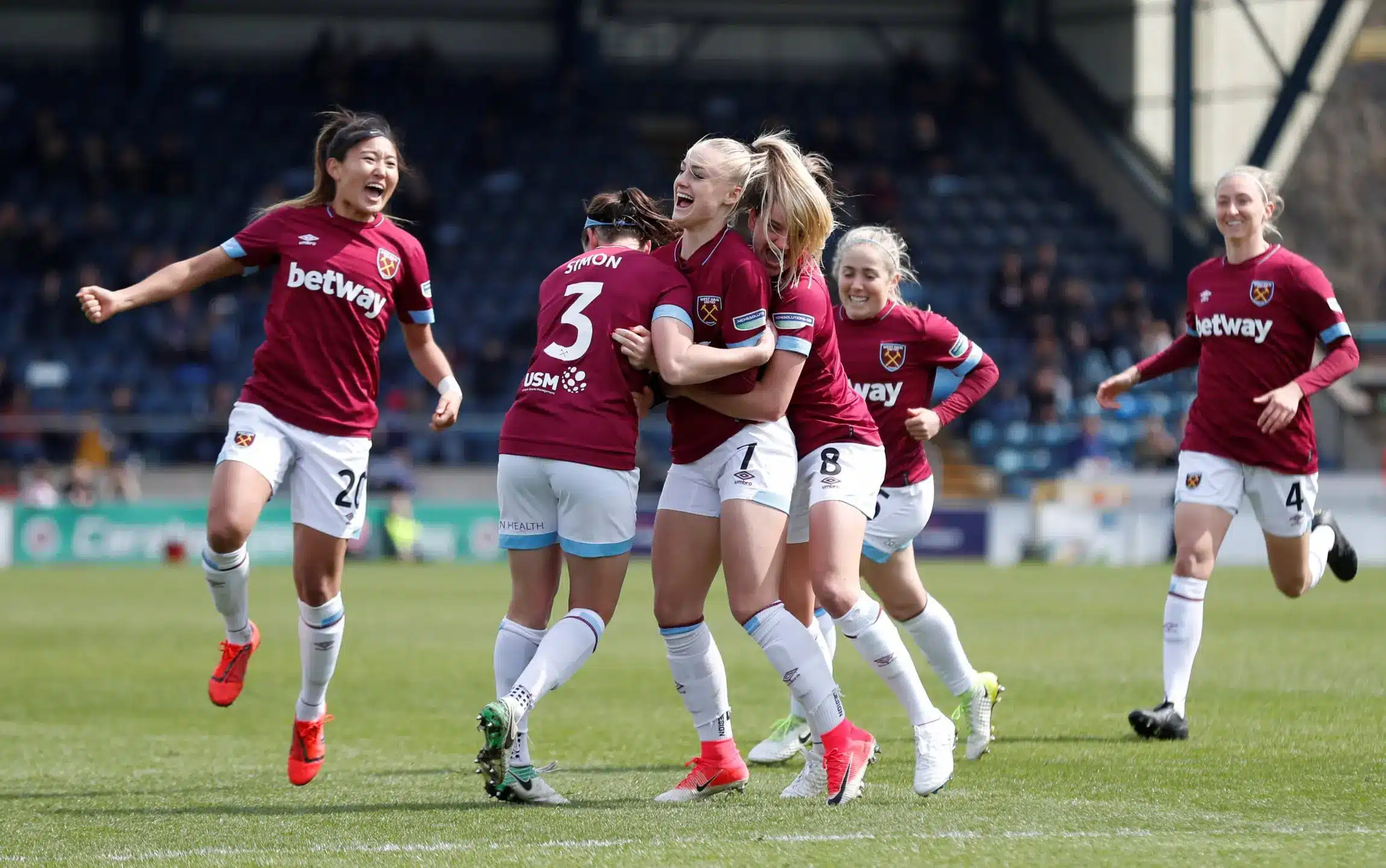 West Ham United Women celebrating a goal during a match, wearing maroon jerseys.