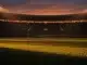 Floodlit stadium at dusk with packed stands, golden-hour lighting, and dramatic shadow patterns across the pitch.