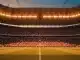 Floodlit stadium at dusk with packed stands showing red/white and navy/white colours; golden hour lighting, low angle perspective.