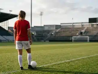 Female footballer viewed from behind on a stadium pitch, symbolising a reported loan move and senior development.